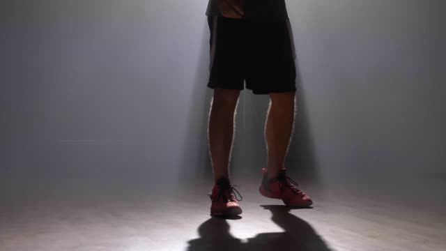 Close-footage-of-basketball-player's-legs-playing-with-ball-in-dark-misty-room-with-smoke