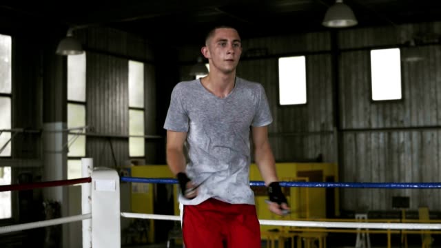 Handsome-young-caucasian-sportsman-is-jumping-with-a-skip-rope-while-working-out-in-boxing-gym,-doing-cross-moves-with-skipping-rope