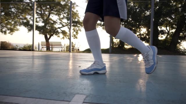Close-up-of-a-female-basketball-player-in-white-golf-socks-and-blue-and-white-sneakers-training-outdoors-on-the-court,-bouncing-a-ball.-No-face.-Close-up