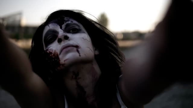 Retrato-de-una-mujer-zombie-espeluznante-con-el-rostro-herido-y-arañar-las-manos-caminando-al-aire-libre-con-un-industrial-lugar-abandonado-en-el-fondo.-Halloween,-concepto-de-filmación,-escalofriante