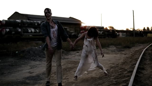 Creepy-two-zombies-in-bloody-clothes-walking-through-the-ruined-city-during-the-zombie-apocalypse.-Abandoned-place-with-trucks-with-missiles-on-the-background