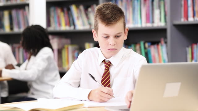 Männlichen-High-School-Schüler-tragen-einheitliche-arbeiten-am-Laptop-In-der-Bibliothek