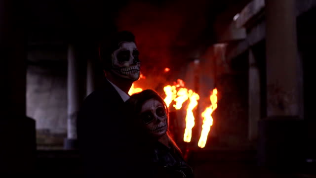 Couple-in-wedding-clothes-and-with-makeup-for-Halloween-stand-near-burning-fire