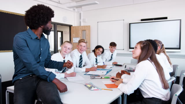 Männlichen-High-School-Lehrer-mit-Teenager-Schüler-tragen-einheitliche-Lehre-Lektion-am-Tisch-sitzen