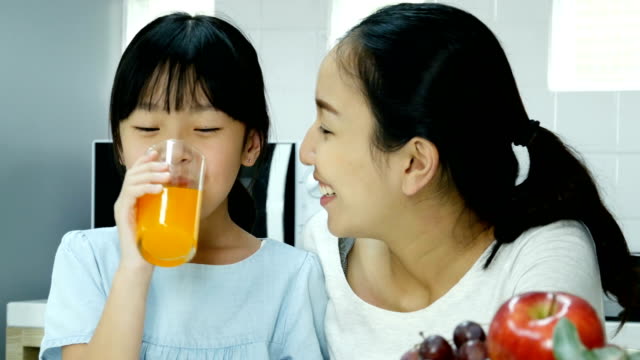 Niña-bebiendo-zumo-de-naranja-con-atractivo-sonriendo-con-su-madre.-Personas-con-estilo-de-vida-y-el-concepto-saludable.