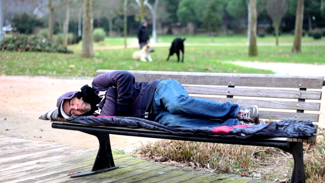 Homeless-man-sleeping-on-bench-at-park