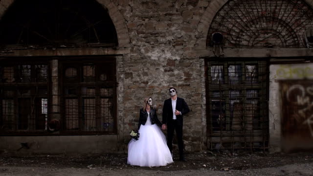 Gruselige-paar-in-ein-Hochzeitskleid-mit-Make-up-für-Halloween-Stand-in-der-Nähe-von-Mauer