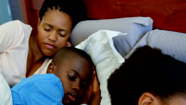 Front-view-of-young-black-family-sleeping-together-on-bed-in-bedroom-of-comfortable-home-4k