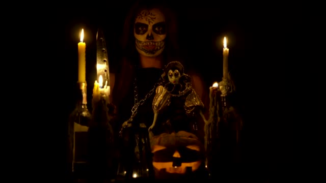 Halloween-witch-with-skull-makeup-makes-voodoo-holds-knife-and-wispering-spell-magic-pumpkin-chains-and-candles