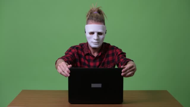 Hipster-Mann-trägt-Maske-als-Hacker-mit-Laptop-gegen-Holztisch