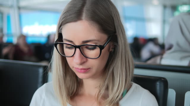 Primer-plano-de-una-joven-con-gafas-trabajando-en-el-ordenador-portátil-en-el-aeropuerto.
