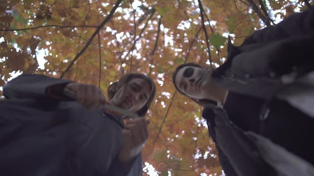 Zwei-Menschen-mit-einer-Luke-in-Halloween-Kostümen,-die-mit-ernsten-gruselnden-Gesichtern-im-Herbstpark-auf-das-Opfer-herabschauen