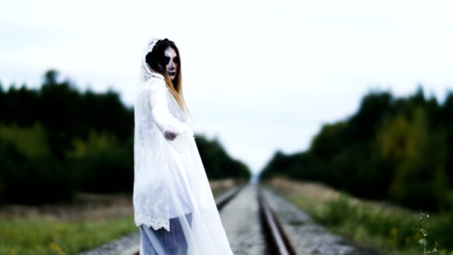 Eine-Frau-mit-Make-up-von-toten-Braut-für-Halloween-in-Hochzeitskleid-auf-den-Schienen.-4K