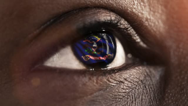 Woman-black-eye-in-close-up-with-the-flag-of-North-Dakota-state-in-iris,-united-states-of-america-with-wind-motion.-video-concept