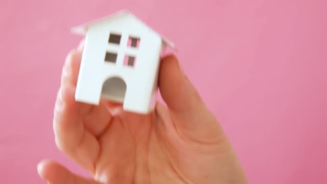 Simply-design-female-woman-hand-holding-miniature-white-toy-house-isolated-on-pink-pastel-colorful-trendy-background