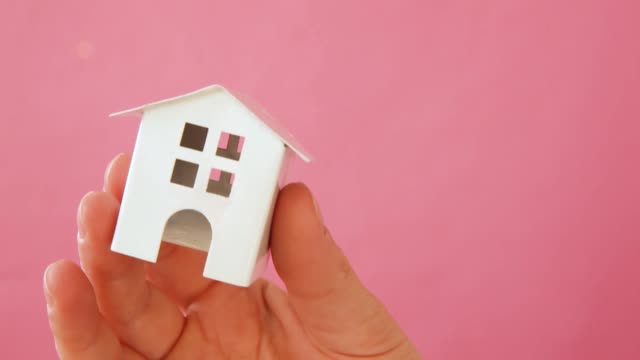 Einfach-Design-weibliche-Frau-Hand-halten-Miniatur-weißes-Spielzeug-Haus-isoliert-auf-rosa-Pastell-bunten-trendigen-Hintergrund