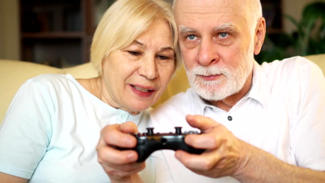 Jugadores-Senior-pareja-jugar-video-juegos-en-casa.-Jugadores-con-mando-de-consola
