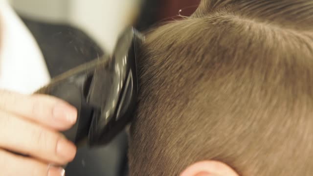 Weibliche-Hand-männliche-Haare-schneiden-mit-Clipper-und-Kamm-in-Friseur-Salon-hautnah.-Friseur-Frisur-mit-elektrischen-Rasierapparat-zu-tun