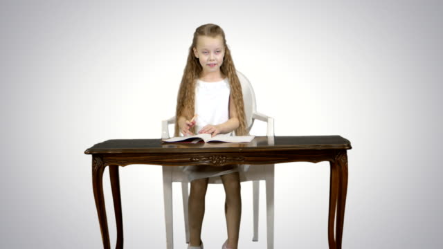 Cute-little-girl-doing-homework,-writing-down-on-white-background