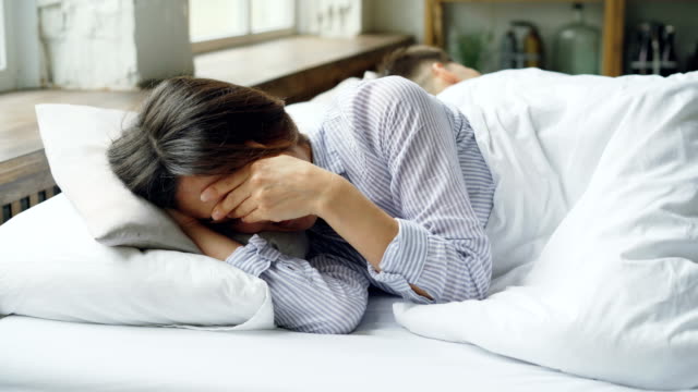 Traurige-Frau-ist-Pyjamas-im-Bett-liegend-und-weinend-nach-Kampf-mit-ihrem-Mann,-der-neben-ihr-mit-dem-Rücken-zu-ihr-liegt.-Schwierigkeiten-im-Eheleben-Konzept.