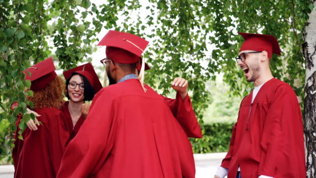 Joyful-boys-and-girls-graduates-in-gowns-and-hats-are-hugging-congratulating-each-other-on-graduation,-laughing-and-having-fun.-Higher-education-and-success-concept.