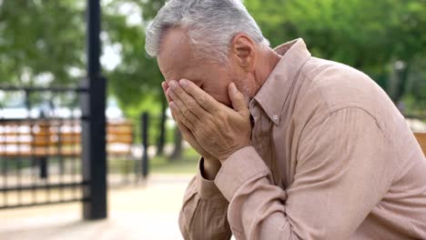 Sad-old-man-sitting-on-hospital-garden-bench,-pensioner-crying-in-sorrow