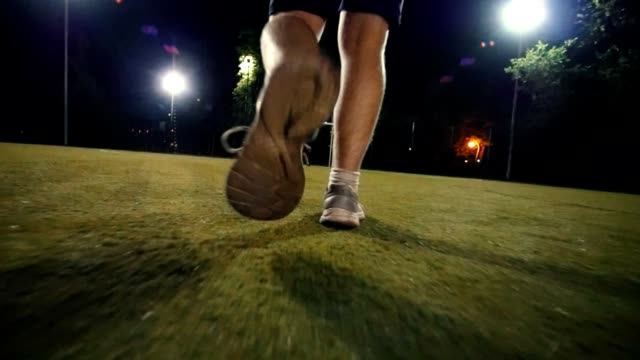 Man-in-sneakers-walks-to-the-ball-and-puts-his-foot-on-the-ball,-night-shooting-on-the-football-field