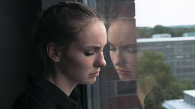 Sad-Young-Woman-Leaning-Head-Against-Glass-Window