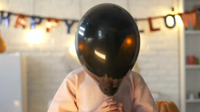Pretty-little-child-hiding-behind-black-balloon-and-showing-claws,-Halloween