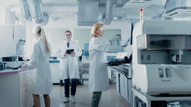 Team-von-Forschern-arbeiten-am-Computer,-mit-medizinischen-Geräten,-Blut-und-genetische-Materialproben-mit-Spezialmaschinen-im-modernen-Labor-analysieren.