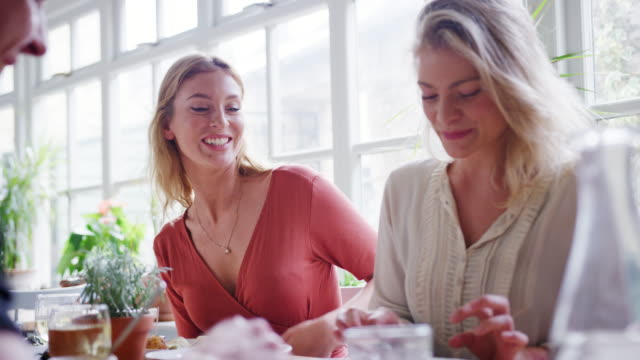 Dos-mujeres-blancas-adultos-jóvenes-comer-el-almuerzo-con-amigos-en-un-restaurante,-de-bajo-ángulo
