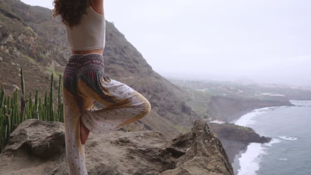 Mujer-joven-haciendo-yoga-en-la-montaña-en-una-isla-con-vista-al-mar,-sentada-en-una-piedra-en-la-cima-de-una-montaña-meditando-en-posición-de-loto