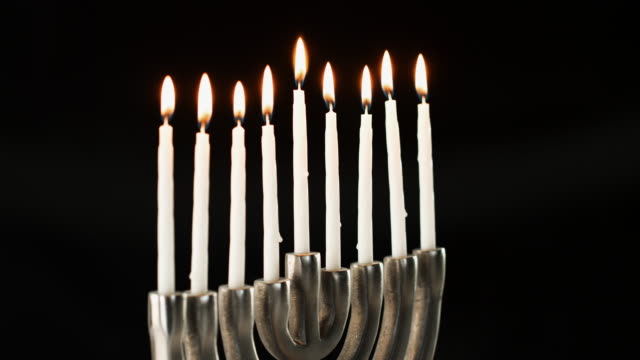 Silver-menorah-with-nine-white,-lit-candles-burning-in-it,-seen-at-an-angle,-close-up,-lockdown