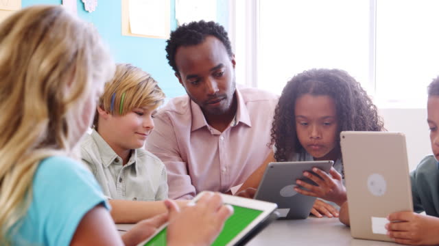 Teacher-helping-kids-using-tablet-in-elementary-school-class
