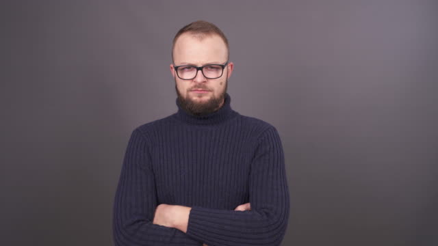 Portrait-of-young-man-with-beard-and-glasses.-Looking-at-camera-with-anger-and-waving-his-arms.-Isolated-on-grey-background.