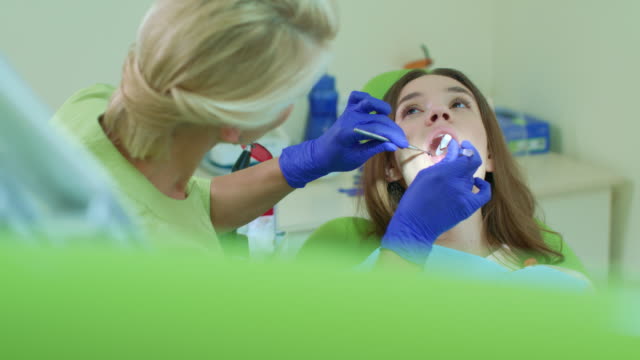 Dentist-putting-cotton-tampon-into-open-patient-mouth.-Dental-treatment-process