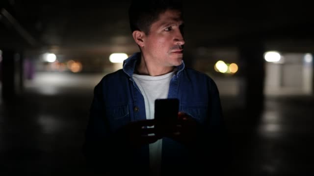 Suspicious-looking-Hispanic-man-thinking-while-using-phone-in-dark-parking-lot