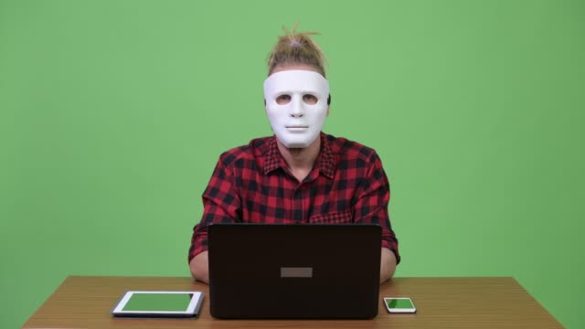 Hipster-Mann-trägt-Maske-als-Hacker-gegen-Holztisch