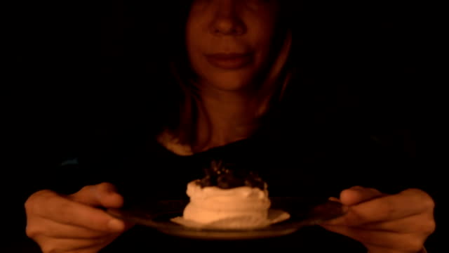 Close-up-of-a-contented-girl-magician-in-a-dark-room-by-candlelight-conjured-herself-a-cake.-Holds-a-plate-of-cake-Low-key-live-camera.
