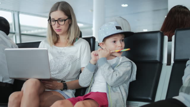Junge-Mutter-arbeitet-auf-Laptop-am-Flughafen-mit-Kind-genießen-Lutscher.