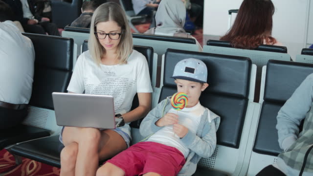 Junge-Mutter-arbeitet-auf-Laptop-am-Flughafen-mit-Kind-genießen-Lutscher.