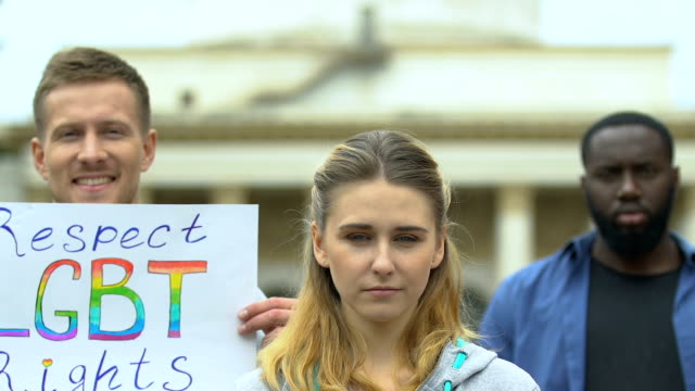 Young-people-raising-banners-with-LGBT-rainbow-heart-and-slogans,-pride-march