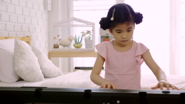 4K:-Asiatische-Skid-Mädchen-trainiert,-um-ein-E-Piano-zu-spielen.-Ist-eine-Aktivität,-die-emotionale-Fähigkeiten-trainiert-Und-der-Körper-gut-studieren-zu-Hause-oder-Musikschule-Musik.-gute-psychische-Gesundheit-und-gute-Laune.