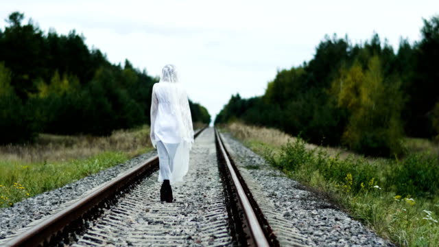 Eine-Frau-im-Hochzeitskleid,-die-entlang-der-Eisenbahn-im-Wald-weggeht.-4K