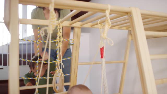 Asiatische-Mutter-Blick-nach-Twin-Kleinkinder-spielen-auf-Home-Gym