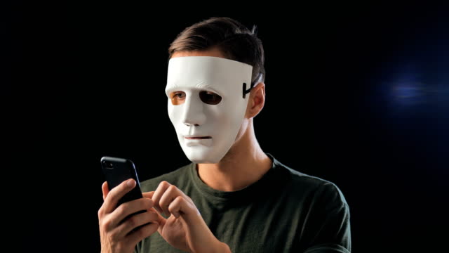 El-estafador-enmascarado-anónimo-exige-un-rescate-por-chantaje-usando-un-teléfono-inteligente.-Masked-Criminal-intimida-a-la-víctima-con-la-ayuda-de-amenazas-a-través-de-SMS-utilizando-el-teléfono-móvil.