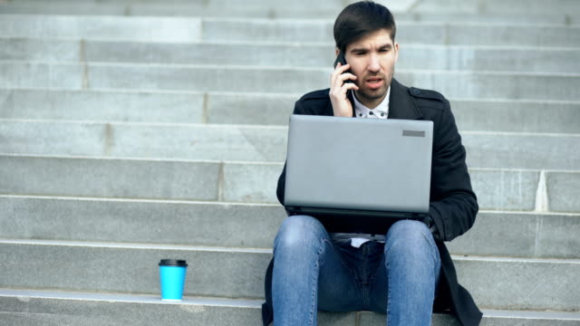 Junger-Geschäftsmann-mit-Laptop-Computer-mit-Stress-nach-dem-Anruf-und-sitzt-auf-der-Treppe-in-der-Straße.-Geschäftsmann-viel-Probleme-bei-Work-Konzept