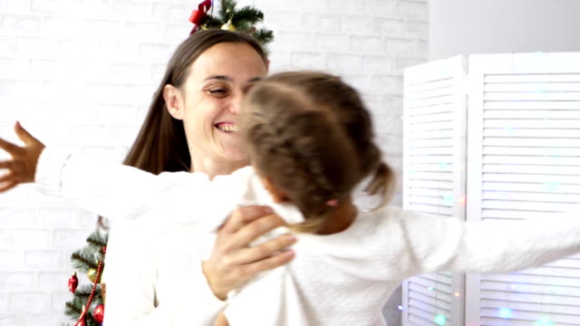 Junge-Mutter-dreht-sich-ihre-kleine-Tochter-mit-Weihnachtsbaum-im-Hintergrund