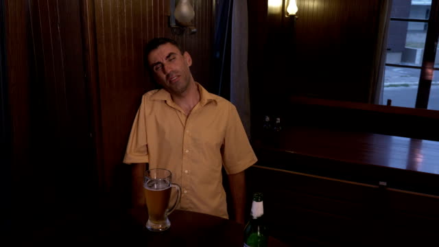 Betrunkener-Mann-einen-Tisch-in-einer-Kneipe-sitzen-halten-nicht-sein-Glas-mit-Bier.