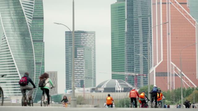 Bike-city-events-competition-in-background-of-skyscrapers,-crowd-of-cyclists-from-thousands-of-people-riding-bicycles,-unrecognizable-people-in-blur,-timelapse